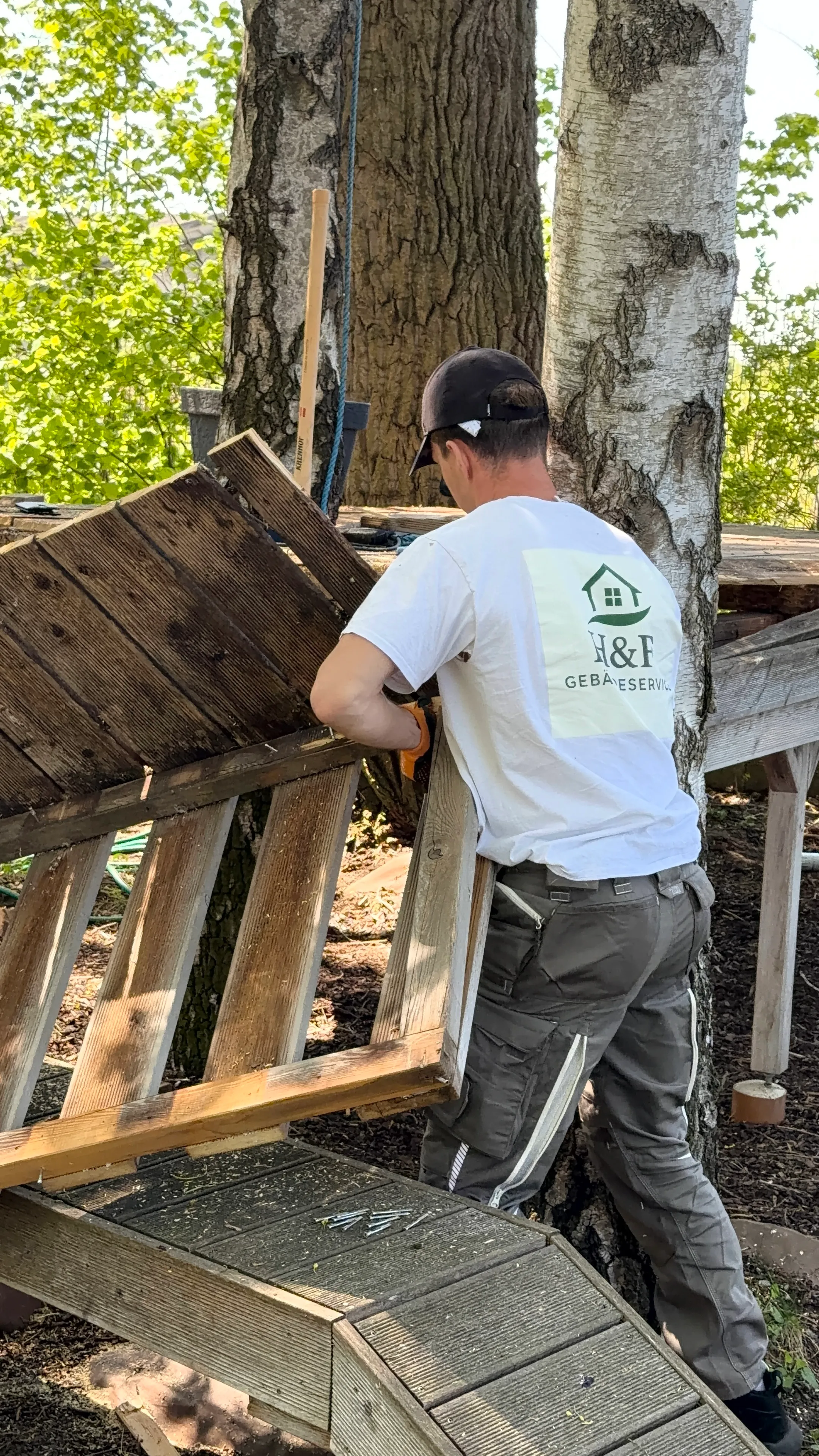 Mitarbeiter von H&F Gebäudeservice zerlegt bei einer Entrümpelung in Wien eine alte Holzkonstruktion im Garten