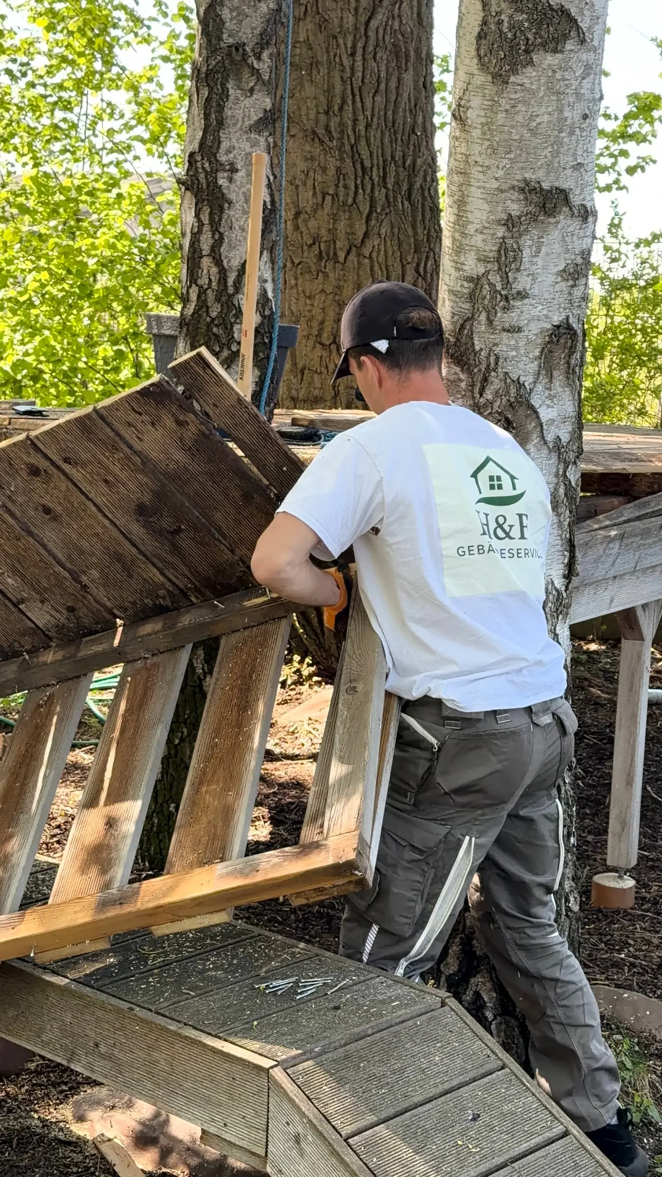 Mitarbeiter von H&F Gebäudeservice zerlegt bei einer Entrümpelung in Wien eine alte Holzkonstruktion im Garten