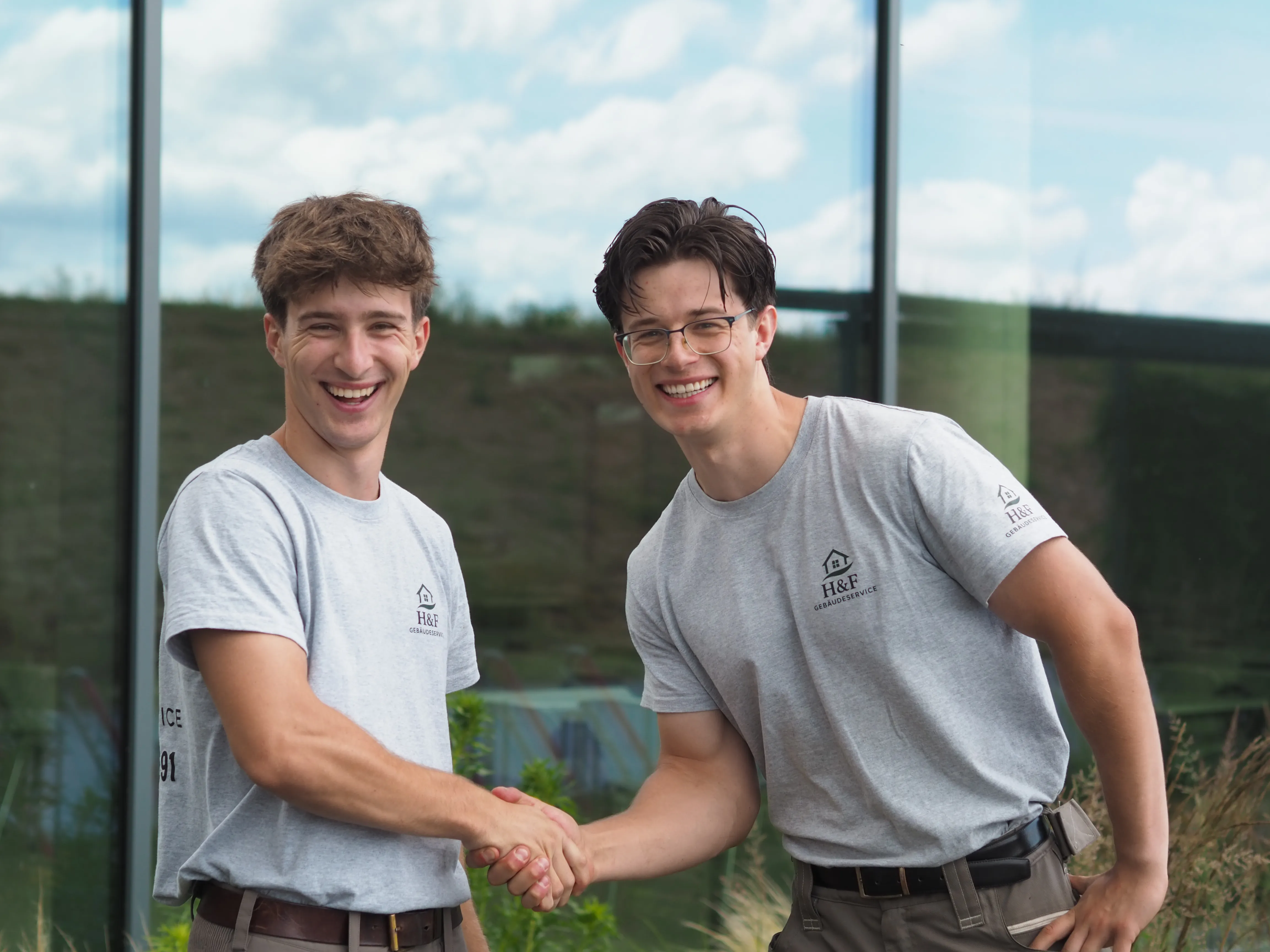 Die Gründer von H&F Gebäudeservice, Max Haustedt und Max Förster, in H&F-Shirts, geben sich lächelnd die Hand